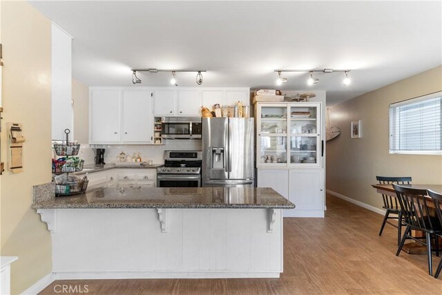 kitchen with stainless steel appliances, a breakfast bar, white cabinets, and kitchen peninsula