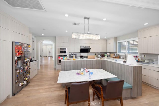 kitchen featuring appliances with stainless steel finishes, decorative light fixtures, a spacious island, and light hardwood / wood-style floors