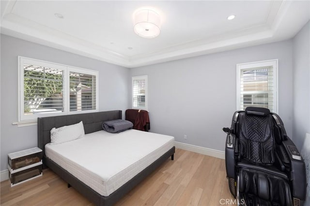 bedroom with light hardwood / wood-style floors, a raised ceiling, and multiple windows