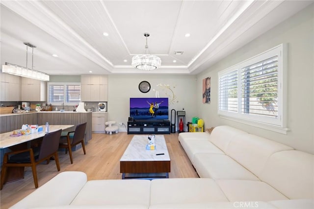 living room featuring a tray ceiling, a wealth of natural light, light wood-type flooring, and ornamental molding