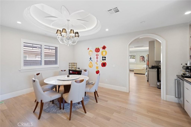 dining space with an inviting chandelier, a raised ceiling, and light hardwood / wood-style floors