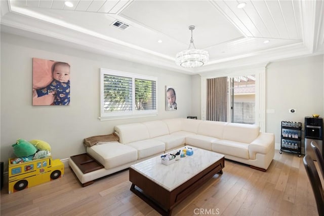 living room featuring a raised ceiling, light wood-type flooring, ornamental molding, and an inviting chandelier