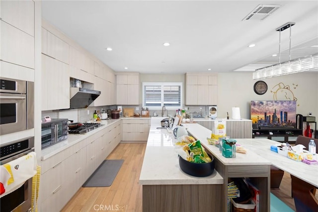 kitchen featuring hanging light fixtures, backsplash, appliances with stainless steel finishes, a kitchen island, and light wood-type flooring