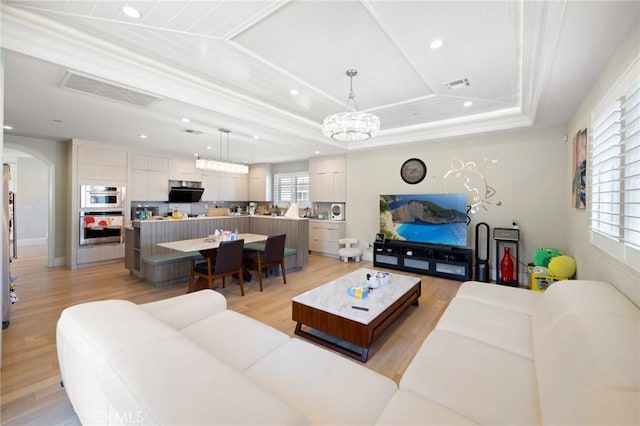 living room featuring a notable chandelier, light hardwood / wood-style floors, ornamental molding, and a tray ceiling