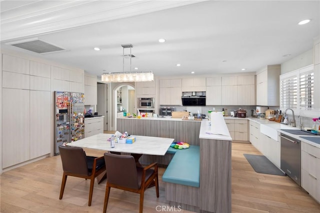 kitchen with a large island, stainless steel appliances, decorative light fixtures, and light wood-type flooring