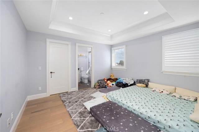 bedroom featuring a tray ceiling, ensuite bathroom, crown molding, and light hardwood / wood-style floors