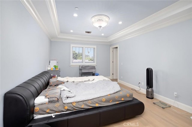 bedroom featuring light hardwood / wood-style floors, crown molding, and a tray ceiling