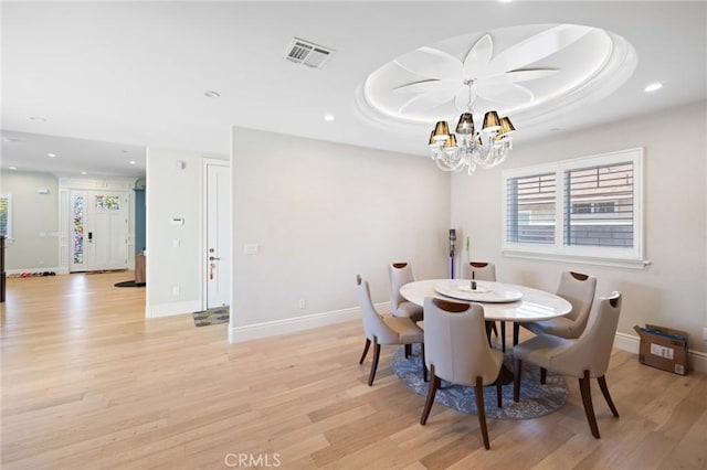 dining space featuring an inviting chandelier, light hardwood / wood-style flooring, and a raised ceiling