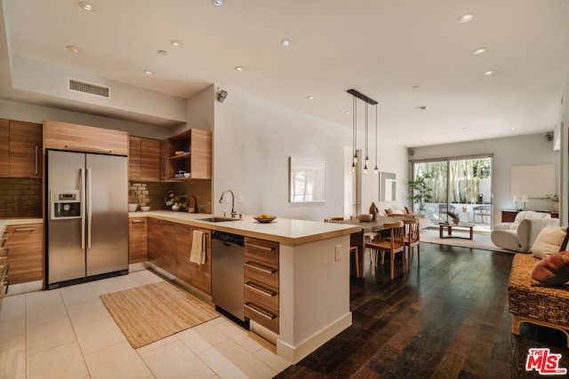 kitchen featuring sink, appliances with stainless steel finishes, tasteful backsplash, decorative light fixtures, and kitchen peninsula