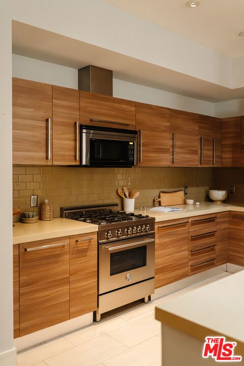 kitchen featuring light tile patterned flooring, high end stove, and backsplash