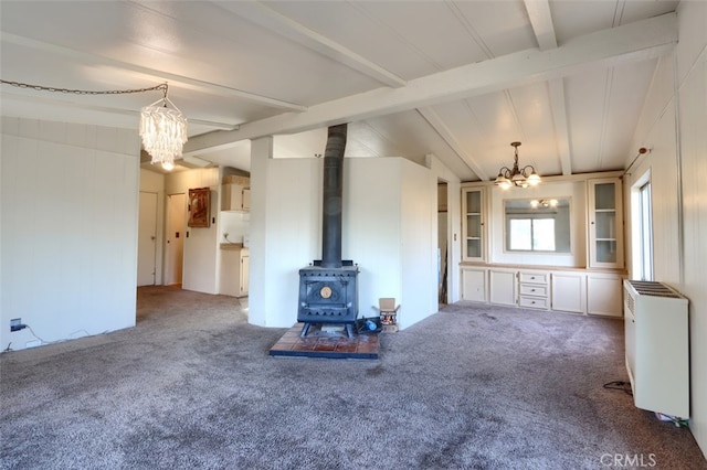 unfurnished living room featuring a wood stove, radiator, an inviting chandelier, lofted ceiling with beams, and carpet floors