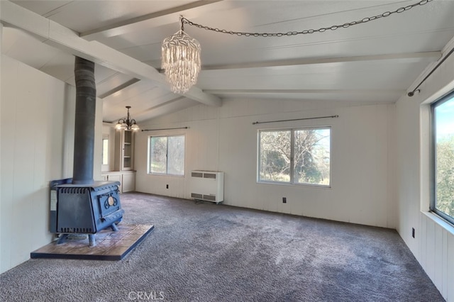 unfurnished living room with a wood stove, radiator heating unit, an inviting chandelier, lofted ceiling with beams, and carpet