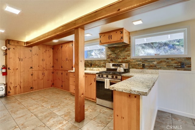 kitchen with light stone countertops, stainless steel gas range oven, backsplash, kitchen peninsula, and wood walls