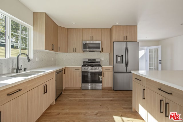 kitchen with appliances with stainless steel finishes, light brown cabinetry, tasteful backsplash, sink, and light hardwood / wood-style flooring