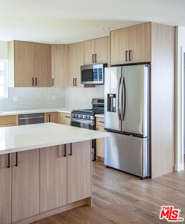 kitchen featuring decorative backsplash, light brown cabinets, light wood-type flooring, and appliances with stainless steel finishes