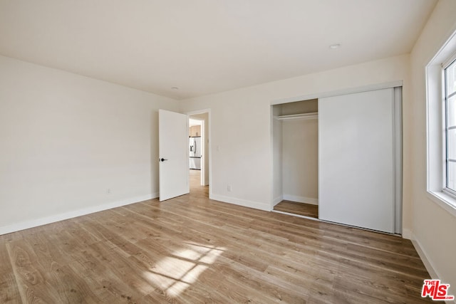 unfurnished bedroom with multiple windows, stainless steel fridge, a closet, and light hardwood / wood-style floors