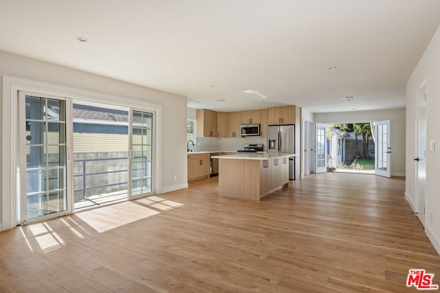 kitchen featuring appliances with stainless steel finishes, tasteful backsplash, light brown cabinets, a center island, and light hardwood / wood-style floors