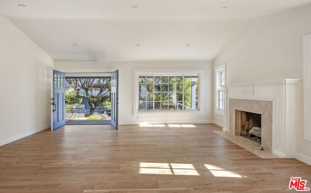 unfurnished living room with a high end fireplace, light hardwood / wood-style floors, and vaulted ceiling