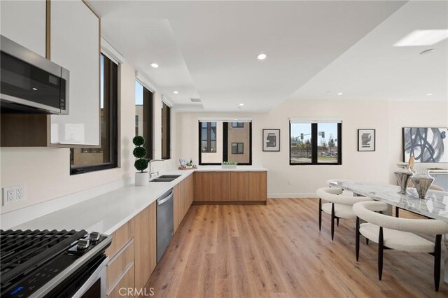 kitchen featuring kitchen peninsula, sink, stainless steel appliances, and light hardwood / wood-style floors