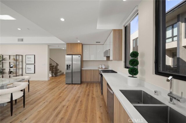 kitchen featuring sink, stainless steel appliances, extractor fan, light hardwood / wood-style floors, and white cabinets