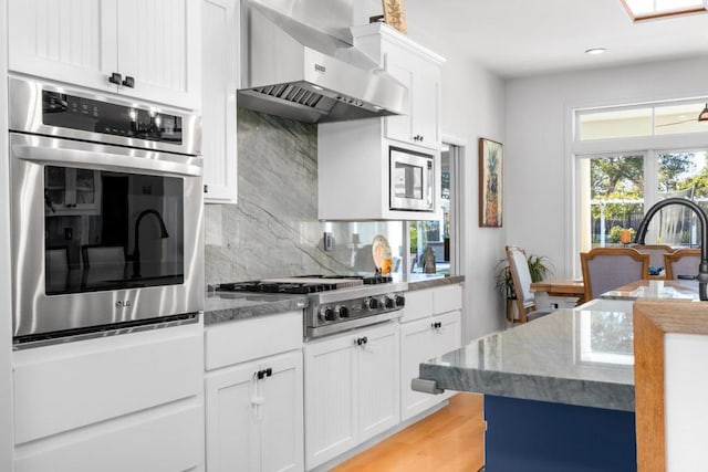 kitchen with white cabinetry, appliances with stainless steel finishes, wall chimney exhaust hood, and decorative backsplash