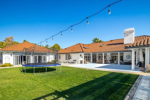 rear view of property featuring a patio, a yard, and a trampoline