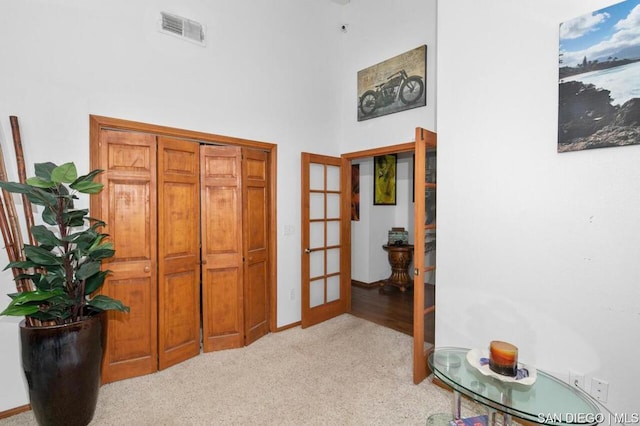 hall featuring a towering ceiling, light carpet, and french doors