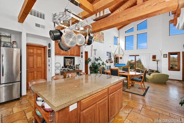 kitchen featuring high vaulted ceiling, beamed ceiling, stainless steel refrigerator, and a center island