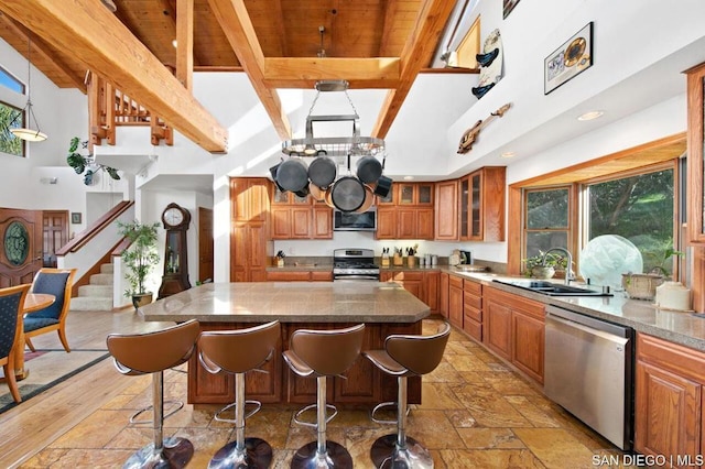 kitchen featuring appliances with stainless steel finishes, a center island, sink, a breakfast bar, and beam ceiling