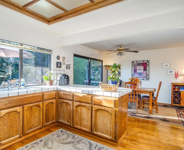 kitchen with ceiling fan, tile countertops, light hardwood / wood-style floors, and kitchen peninsula