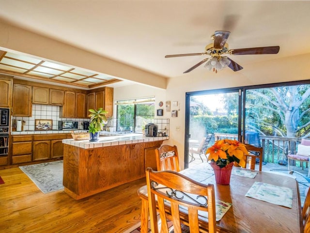 kitchen featuring tile counters, black appliances, wood-type flooring, decorative backsplash, and kitchen peninsula