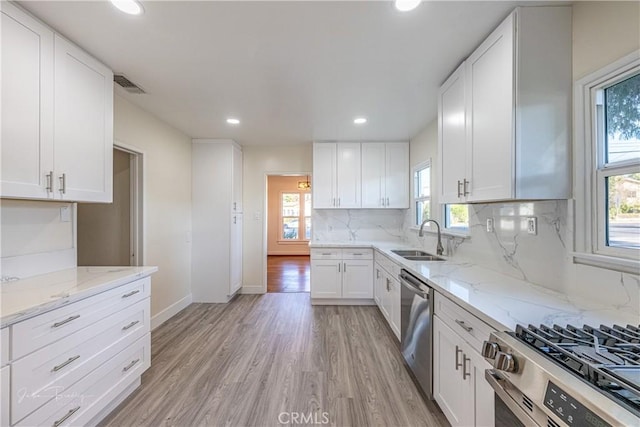 kitchen with sink, light stone countertops, appliances with stainless steel finishes, tasteful backsplash, and white cabinetry