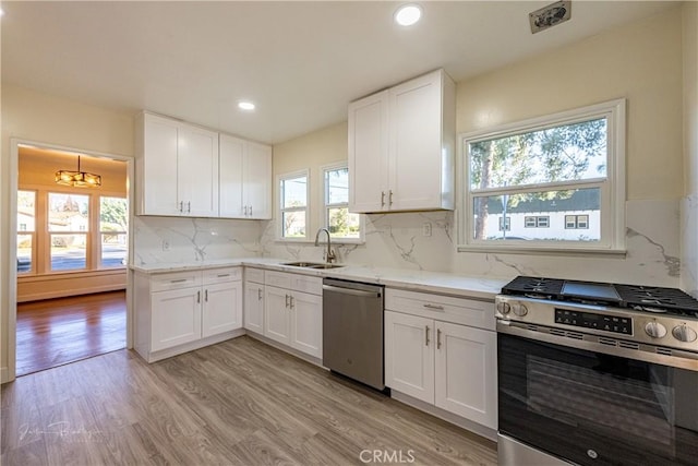 kitchen with appliances with stainless steel finishes, light wood-type flooring, backsplash, sink, and white cabinetry