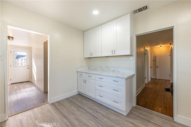 kitchen with white cabinets, light wood-type flooring, and light stone countertops