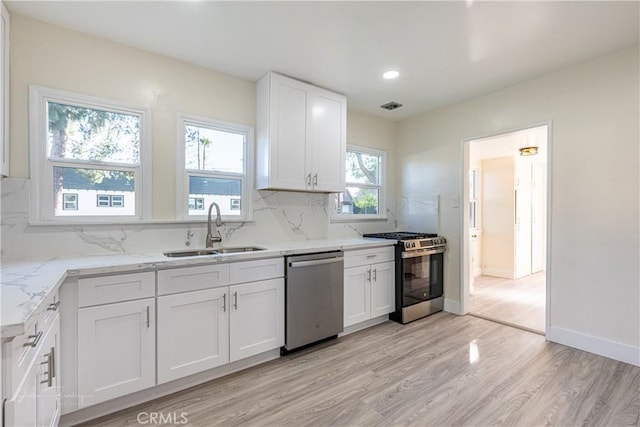 kitchen featuring light stone countertops, appliances with stainless steel finishes, sink, light hardwood / wood-style flooring, and white cabinetry