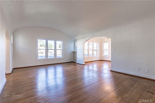 spare room with lofted ceiling, brick ceiling, a wealth of natural light, and dark wood-type flooring