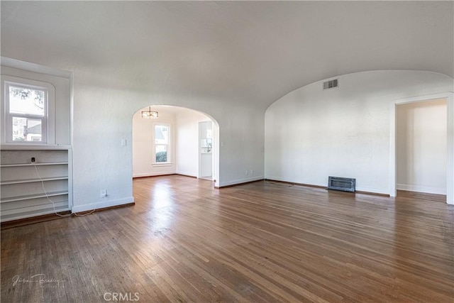 unfurnished living room featuring vaulted ceiling, plenty of natural light, dark wood-type flooring, and brick ceiling