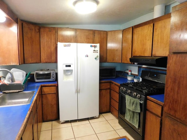 kitchen with gas stove, extractor fan, sink, white refrigerator with ice dispenser, and light tile patterned floors