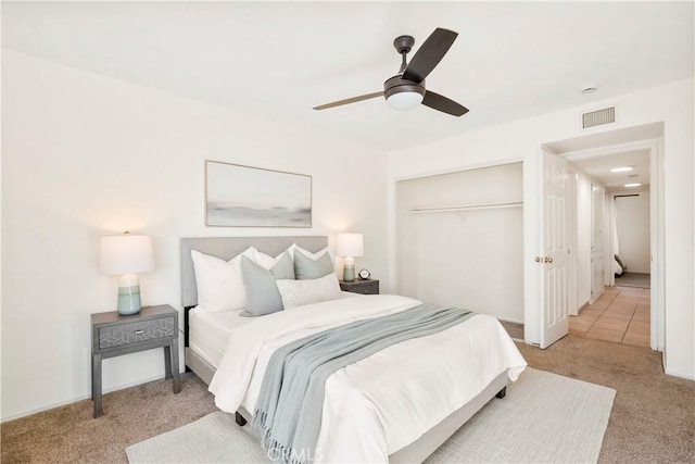 bedroom featuring light colored carpet, ceiling fan, and a closet