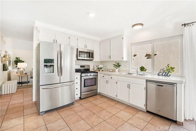 kitchen with sink, light tile patterned floors, radiator, appliances with stainless steel finishes, and white cabinets