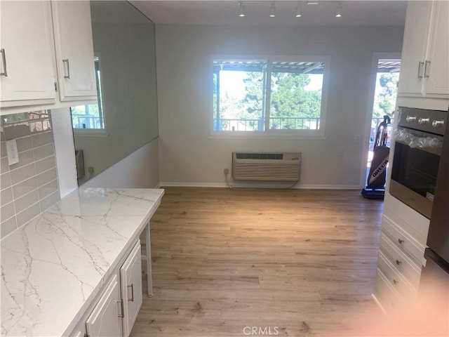 kitchen featuring stainless steel oven, white cabinetry, light hardwood / wood-style flooring, a wall unit AC, and light stone counters