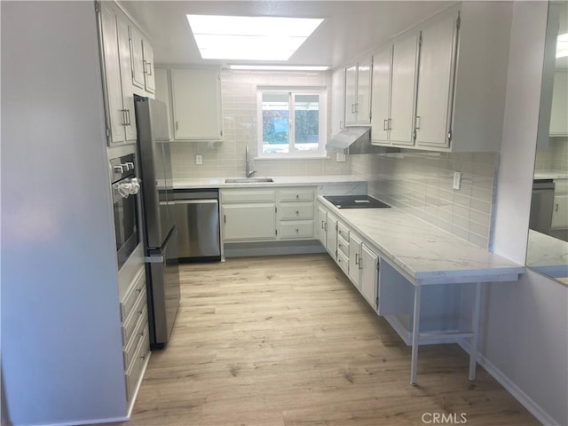 kitchen with white cabinetry, stainless steel appliances, light hardwood / wood-style floors, sink, and backsplash