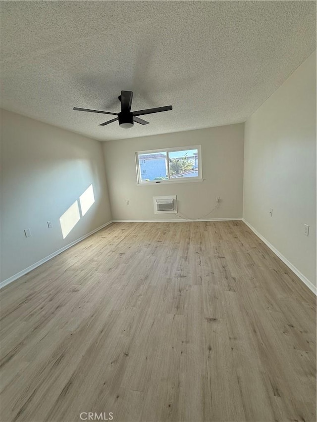 empty room with light hardwood / wood-style floors, a textured ceiling, an AC wall unit, and ceiling fan