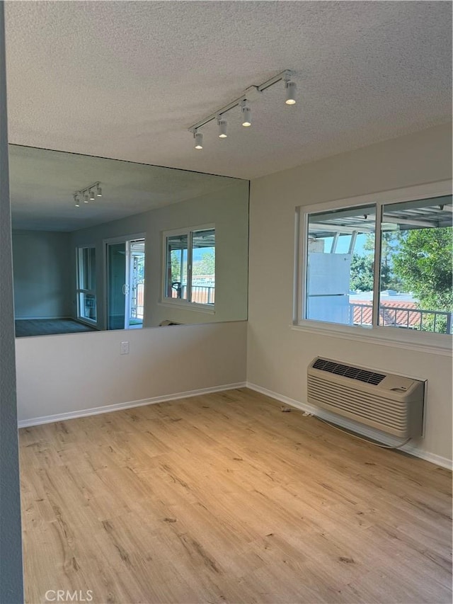 unfurnished room with an AC wall unit, light hardwood / wood-style flooring, and a textured ceiling