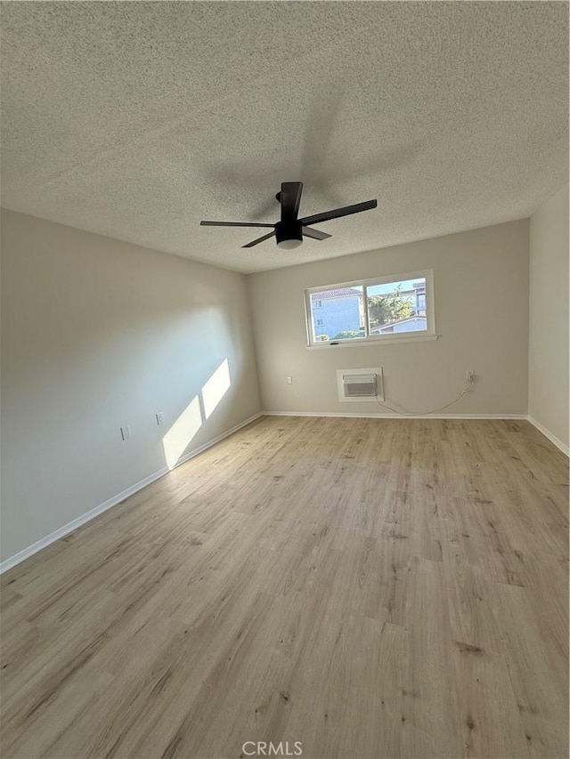 spare room featuring a wall mounted air conditioner, a textured ceiling, ceiling fan, and light wood-type flooring