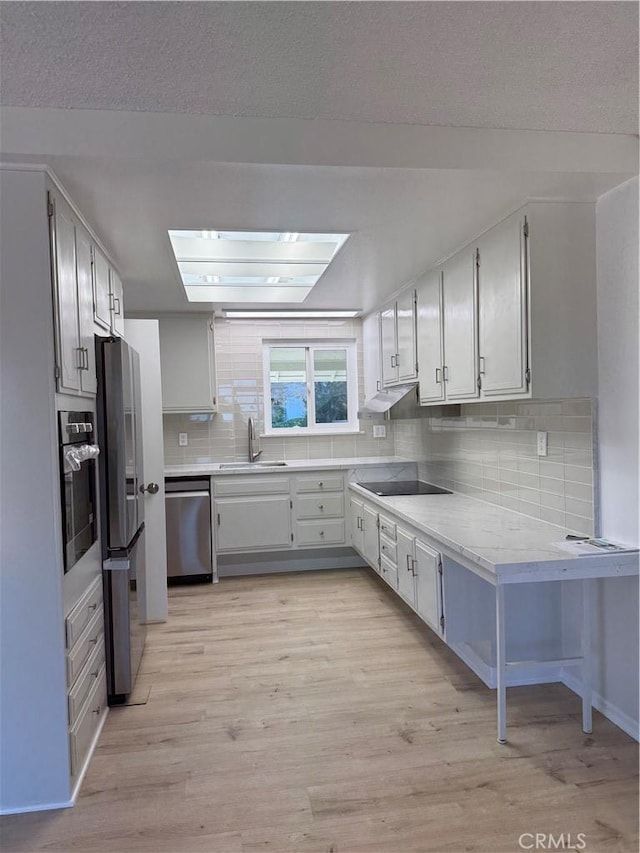 kitchen with light hardwood / wood-style floors, appliances with stainless steel finishes, a textured ceiling, white cabinetry, and sink