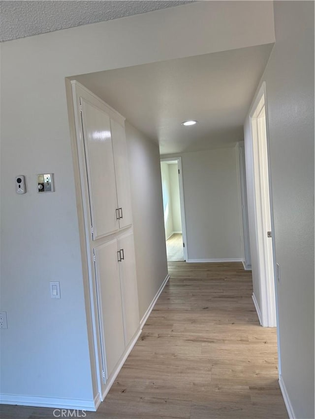 hall with light wood-type flooring and a textured ceiling