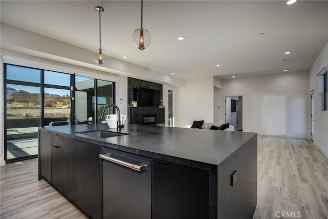 kitchen with decorative light fixtures, sink, an island with sink, and light hardwood / wood-style flooring