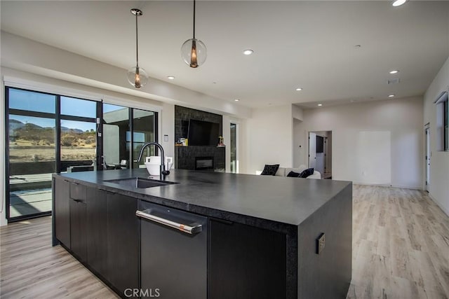 kitchen featuring pendant lighting, sink, a kitchen island with sink, and light wood-type flooring