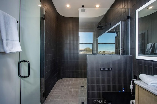 bathroom featuring walk in shower, vanity, and tile walls